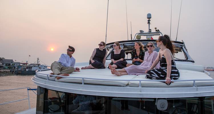 Vrienden ontspannen op het zonnedek van een jacht bij zonsondergang in de buurt van een rivierdorpje.