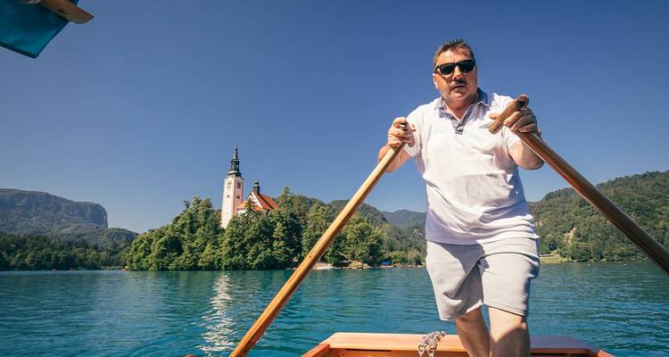 Rameur de style gondolier faisant avancer une barque en bois sur le lac de Bled avec l'île de l'église en arrière-plan.