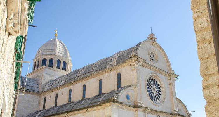 Extérieur du dôme en pierre blanche de la cathédrale de Sibenik et de sa rosace sur fond de ciel dégagé.