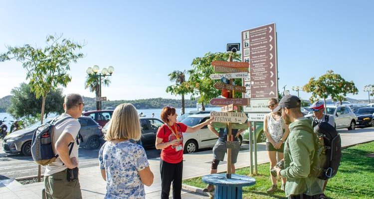 Guide expliquant les panneaux indicateurs aux touristes près de la promenade balnéaire de l'Adriatique avec des voitures garées.