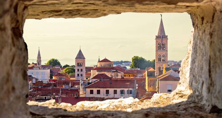 Paysage urbain encadré des tours de cloches de la vieille ville de Zadar vu à travers une fenêtre en pierre ancienne.