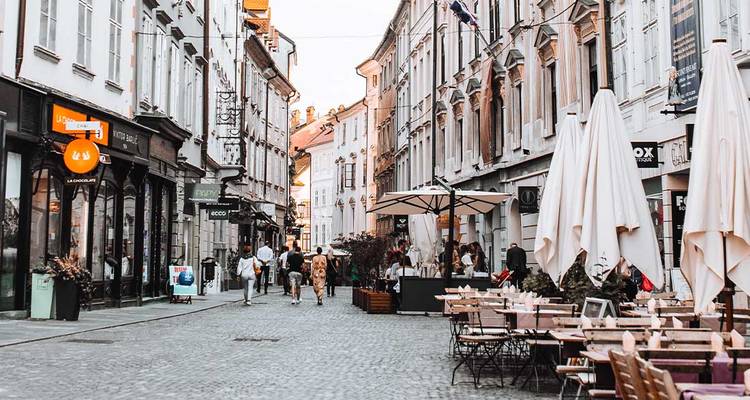 Rue piétonne dans la vieille ville de Ljubljana avec des cafés en plein air, des promeneurs et des façades pastel.