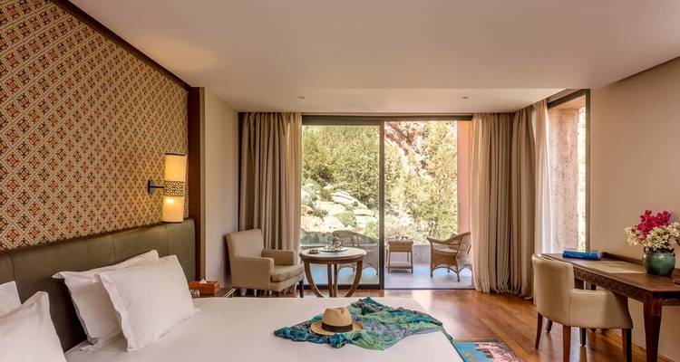 Lichte, elegante hotelkamer met grote glazen deuren die uitkomen op een balkon met uitzicht op weelderige tuinen.