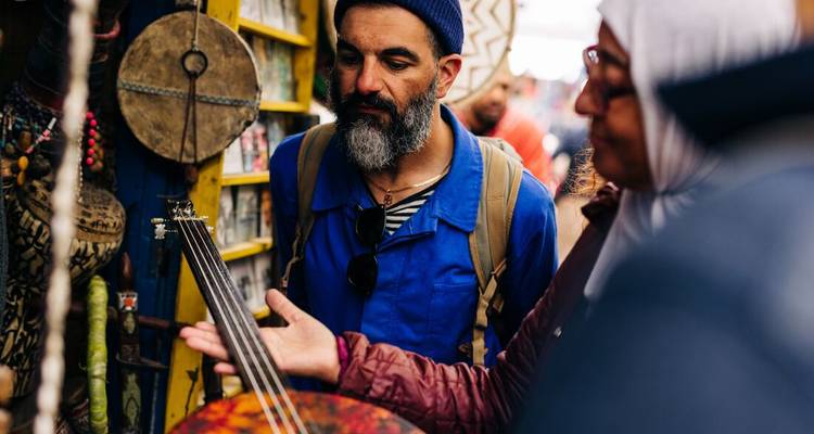 Shoppers die een traditioneel snaarinstrument bekijken in een druk Marokkaanse marktkraam.
