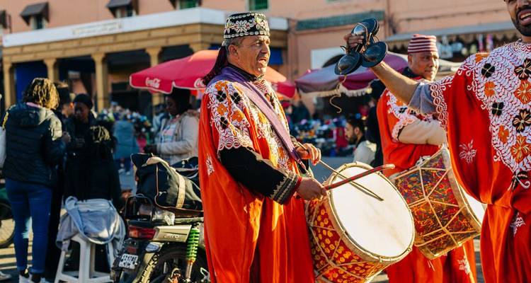 Traditionele muzikanten in levendige oranje gewaden die met trommels en castagnetten optreden op een gezellig plein.
