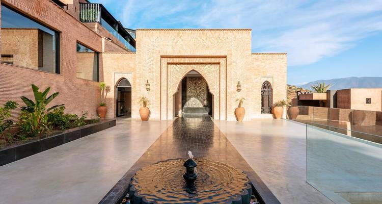 Elegante binnenplaatsingang van een luxe Marokkaanse riad met centrale fontein en sierlijke boogpoort.