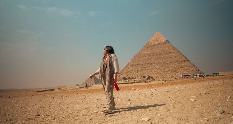 Traveller stands before the pyramids on a vast sandy plain