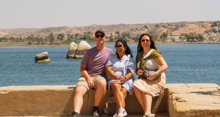 Three travellers pose on riverside stone wall with Nile scenery behind