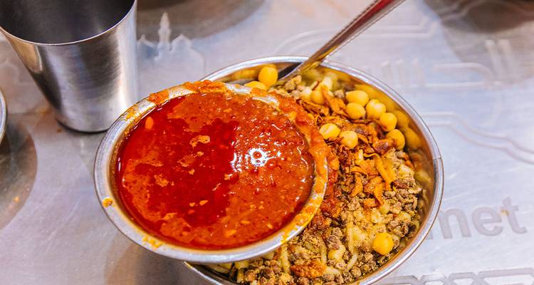Close-up of colourful Egyptian koshari dish topped with spicy tomato sauce
