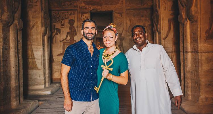 Visitors smile with local guide inside decorated ancient temple holding an ankh