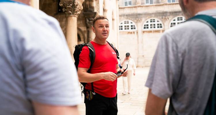 Tour guide in red shirt talks to travellers in a historic stone courtyard