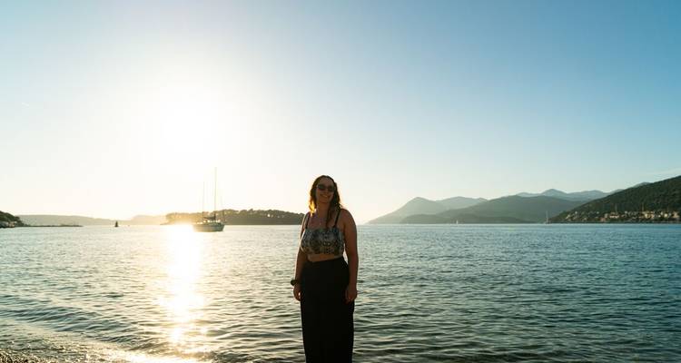 Woman poses on a quiet beach with calm sea and setting sun behind her