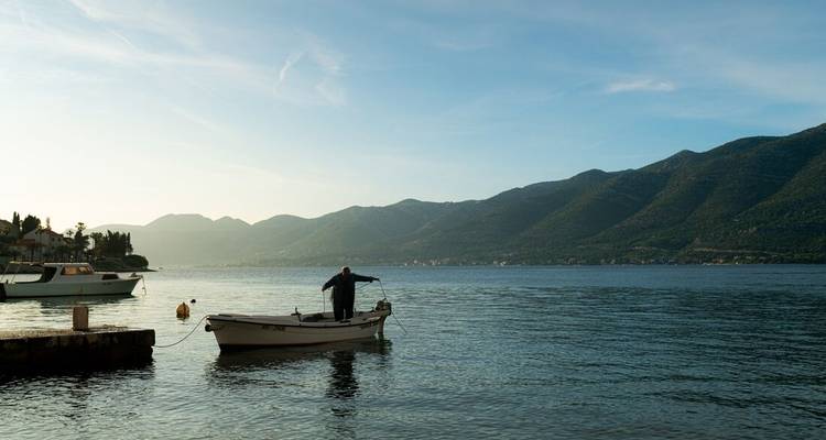 Fisherman stands alone in a small boat on calm coastal waters at dawn