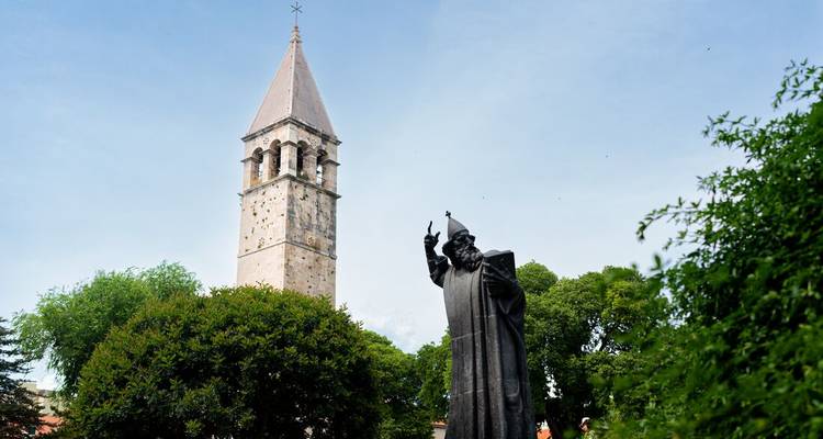 Stone church bell tower and dark bronze statue framed by green trees