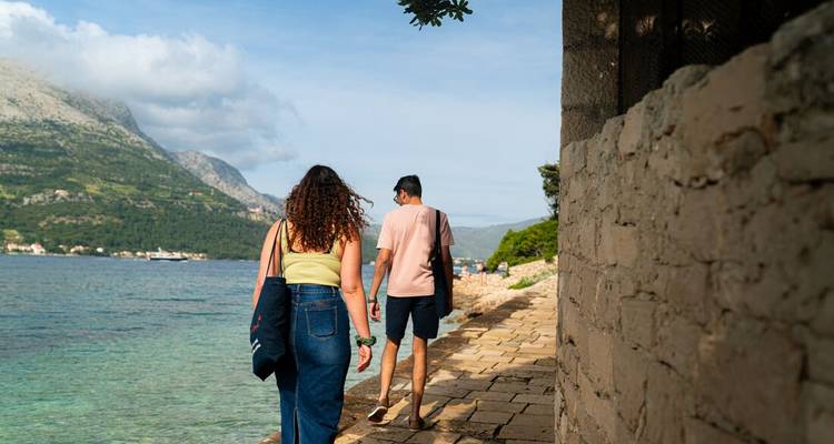 Young couple walk along a stone coastal path beside clear blue water
