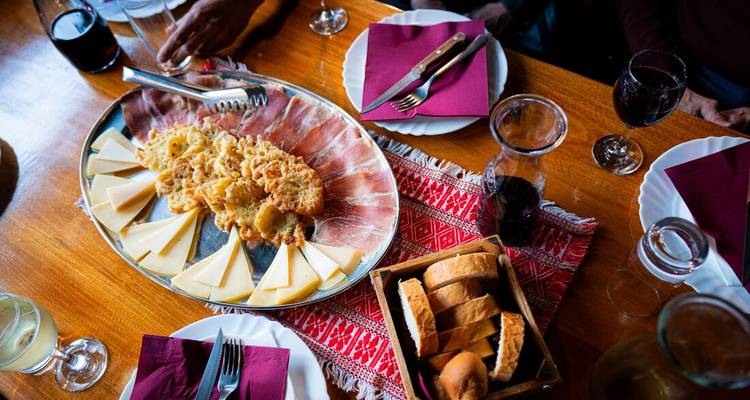 Platter of cheese, prosciutto and fritters with wine glasses on wooden table