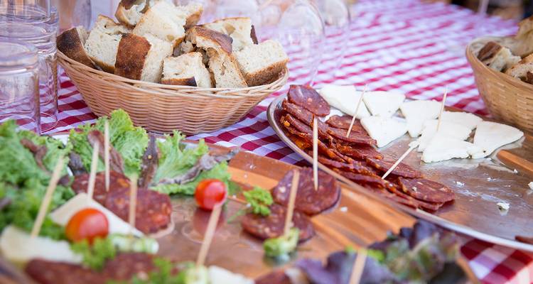 Rustic spread of bread, cured meats and cheese on a checkered tablecloth