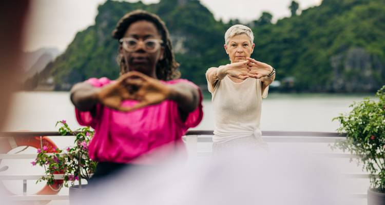 Deux voyageurs pratiquent des exercices d'étirement sur le pont d'une croisière avec les pics calcaires de la baie d'Halong et une eau calme en arrière-plan.