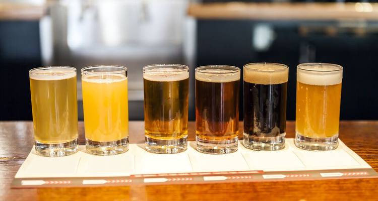 A tasting flight of six different coloured craft beers is lined up on a bar.