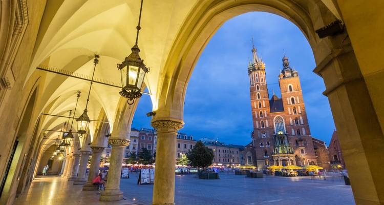 St. Mary’s Basilica towers over Krakow’s Main Square, framed by ornate arches and lanterns at dusk.