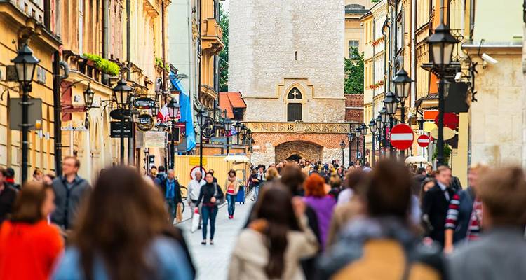 Crowds fill a lively pedestrian street in Krakow’s old town, framed by historic buildings and a stone gate.