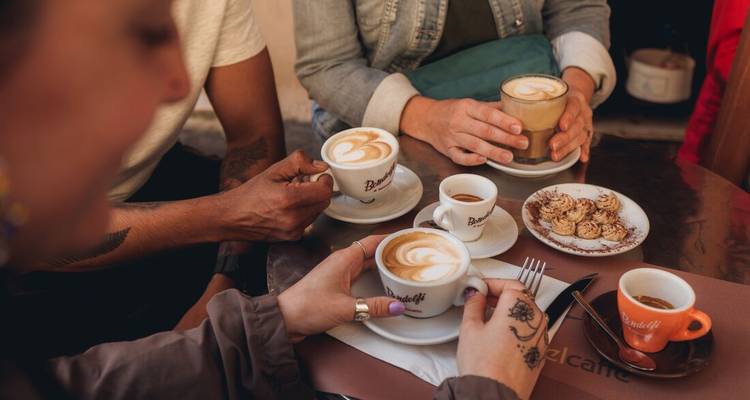 Les mains tiennent des cappuccinos et des expressos sur une table de café, mettant en avant un art du latte mousseux à côté des pâtisseries.