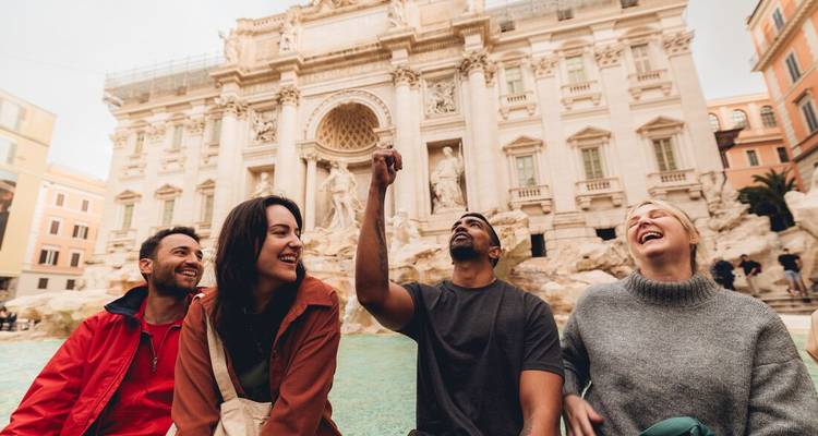 Quatre amis rient ensemble devant la Fontaine de Trevi à Rome, jetant des pièces de monnaie dans l'eau.