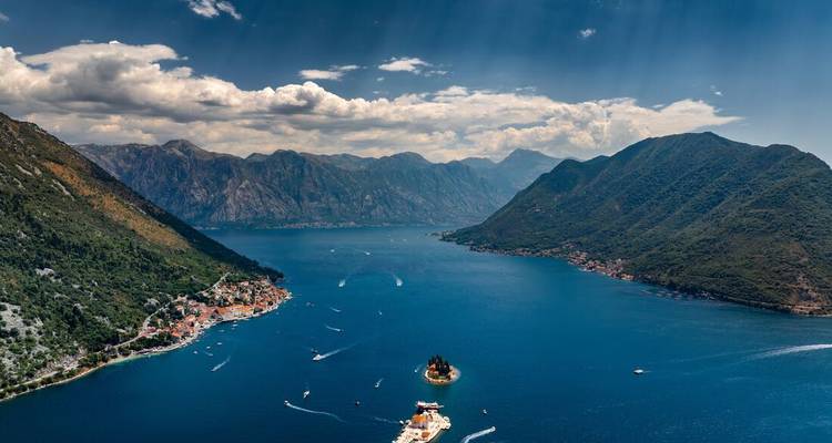 Weitläufiges Luftpanorama der Bucht von Kotor mit tiefblauem Wasser, umgebenden Bergen und winzigen Inselkirchen.