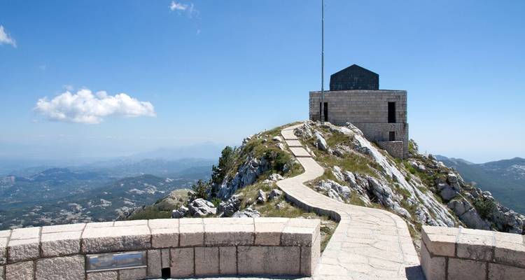 Steinpflaster, das zum Njegoš-Mausoleum auf einem Bergipfel unter einem strahlend blauen Himmel führt.