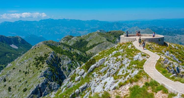 Wanderer, die entlang eines Steinpfades auf einem Bergrücken mit weitreichenden Aussichten auf zerklüftete Gipfel gehen.