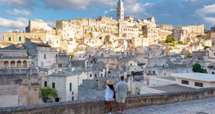 Un couple romantique admirant les habitations en pierre illuminées par le soleil, empilées le long de la colline dorée d'une ancienne ville troglodytique.