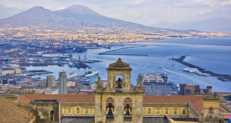 Vue aérienne panoramique du port de Naples avec le Mont Vésuve dominant la ville et la Baie bleue de Naples s'étendant jusqu'à l'horizon.