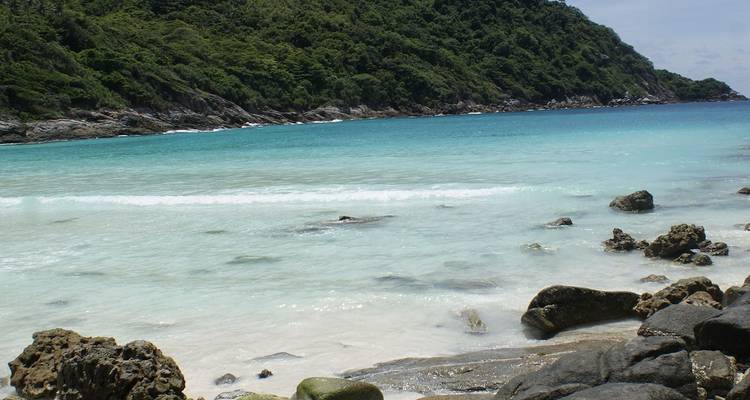 Rotsachtige kust met zachte turkooizen golven die tegen een stille tropische baai klotsen.
