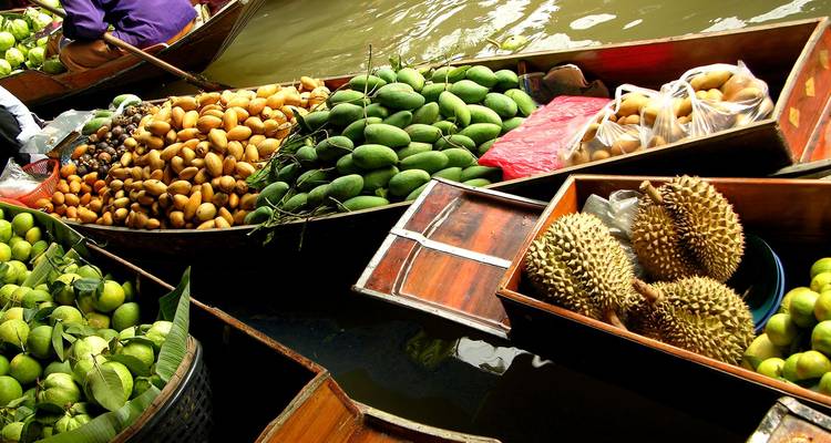 Gamme colorée de fruits tropicaux empilés haut sur des bateaux à longue queue dans un marché flottant animé.