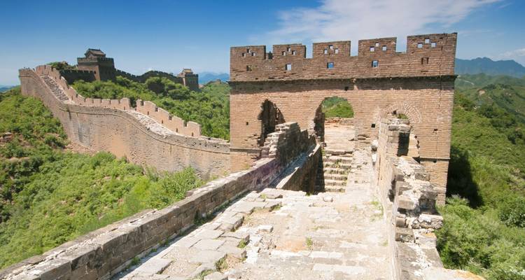 Les anciens remparts de pierre de la Grande Muraille serpentant sur des collines verdoyantes sous un ciel bleu dégagé.
