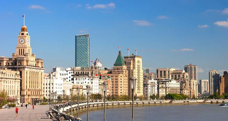 Historische Bund-waterfront met koloniale gebouwen die uitkijken op moderne wolkenkrabbers aan de overkant van de Huangpu-rivier onder een heldere blauwe hemel.