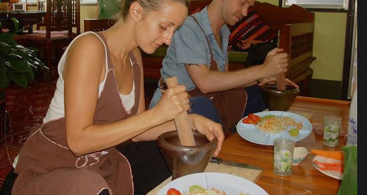 Reizigers die ingrediënten met vijzels fijnmaken tijdens een interactieve Thaise kookles.
