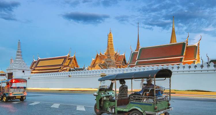 Tuk-tuks rijden langs de witte muren en gouden spitsen van Bangkoks Grand Palace bij zonsondergang