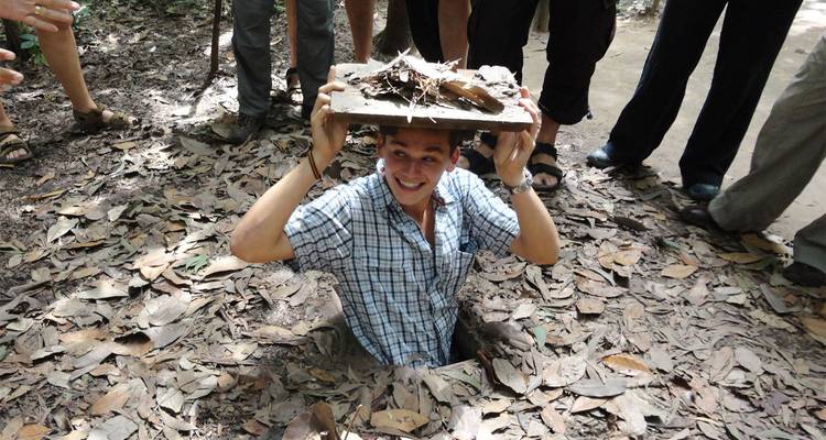 Glimlachende deelnemer demonstreert verborgen ingang van Cu Chi tunnels te midden van gevallen bladeren