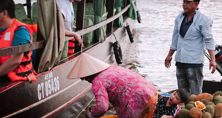 Verkopers in bootjes die tropisch fruit uitwisselen langs een groter toeristenboot op een modderige rivier
