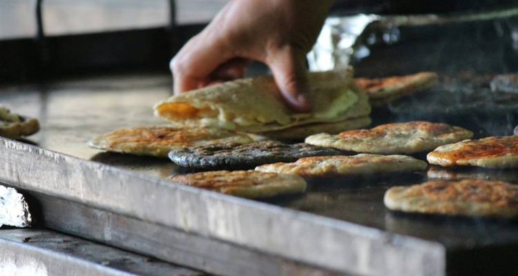 Hand folding a fresh tortilla over sizzling traditional Mexican snacks on a hot griddle.