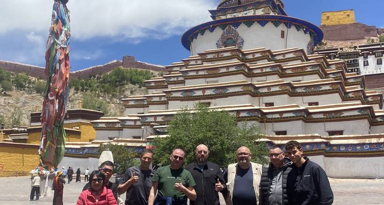 Groupe de voyageurs posant devant le stupa Gyantse Kumbum à plusieurs étages orné de motifs éclatants.