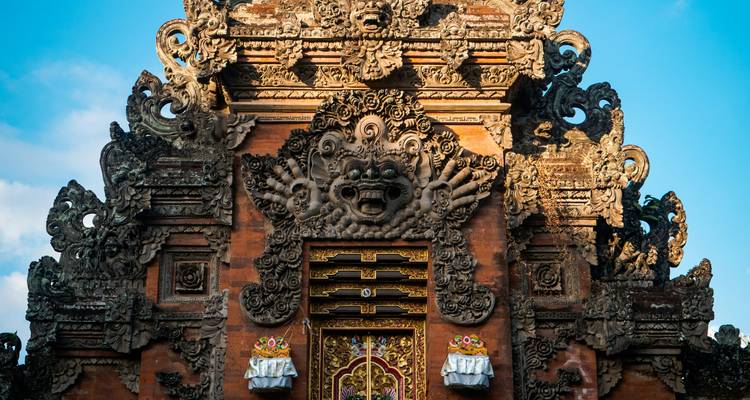 Portail de temple balinais finement sculpté avec des figures tutélaires contre un ciel bleu