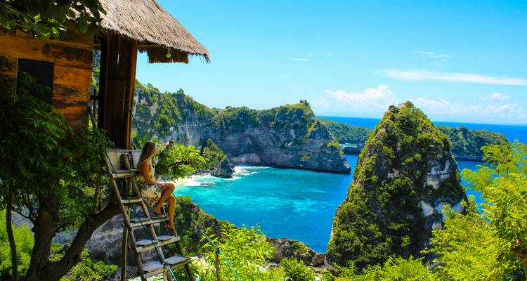 Voyageur sur une échelle de cabane dans les arbres en bois contemplant une baie turquoise spectaculaire et des falaises calcaires