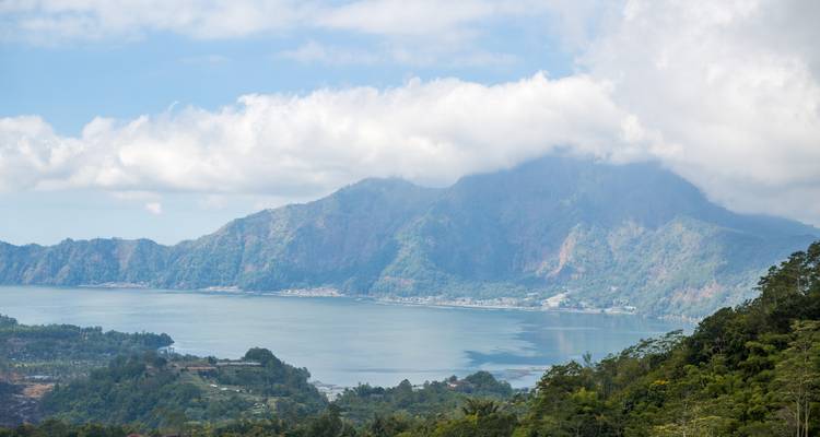 Ruhige Aussicht über den vulkanischen Batur-See, umrahmt von nebelverhangenen Bergen und Wolken.