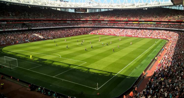 High angle match action inside Emirates Stadium with full crowd and bright afternoon sun.