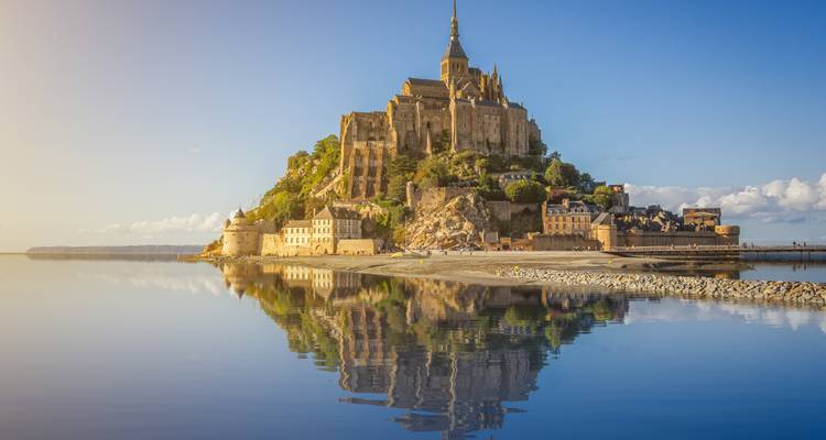 Iconische Mont Saint-Michel abdij die oprijst uit een getijdeneiland, perfect weerspiegeld in rustig water bij zonsopgang.