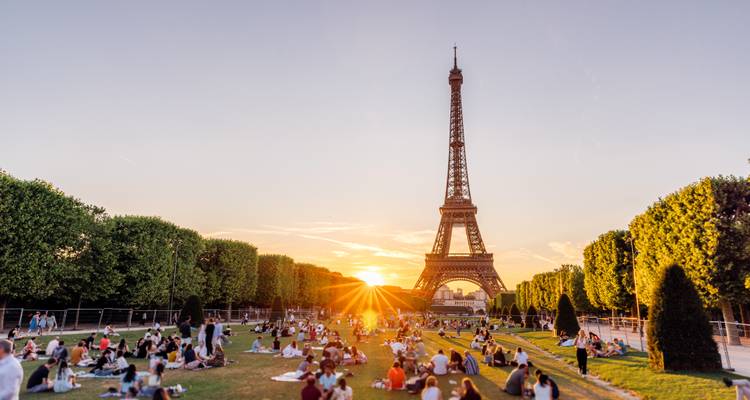 Menigten die zich ontspannen op het groene Champ de Mars terwijl de Eiffeltoren zich verheft tegen een vurige zonsondergang.
