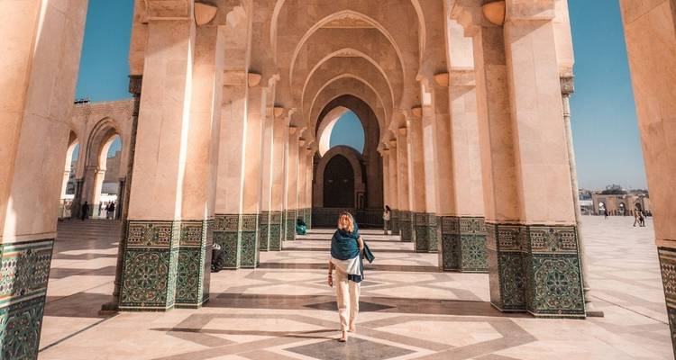 Traveller walking through the grand archways of Hassan II Mosque courtyard with intricate tile work.