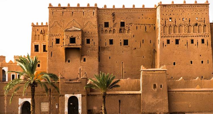 Earthen-walled kasbah fortress with palm trees under a clear blue sky
